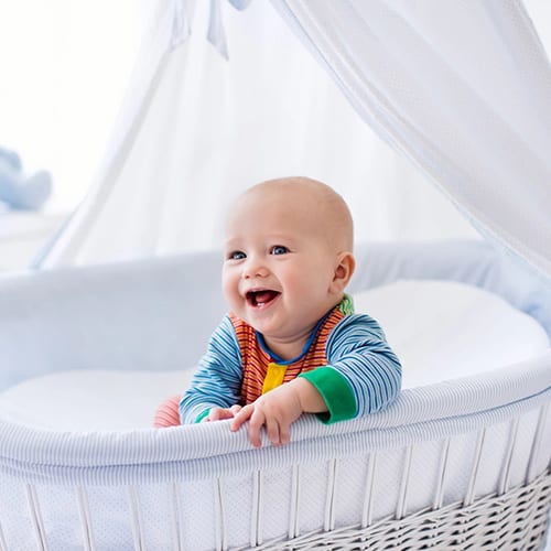 Smiling baby sitting upright in a white bassinet