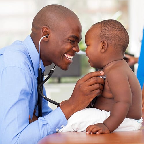 Doctor smiling at a laughing toddler while using a stethoscope to check the baby's heartrate